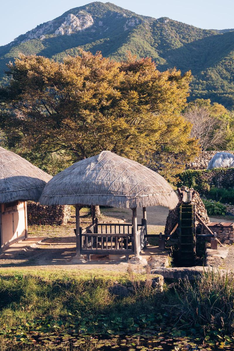 Traditional Korean folk village with thatched-roof houses and mountains