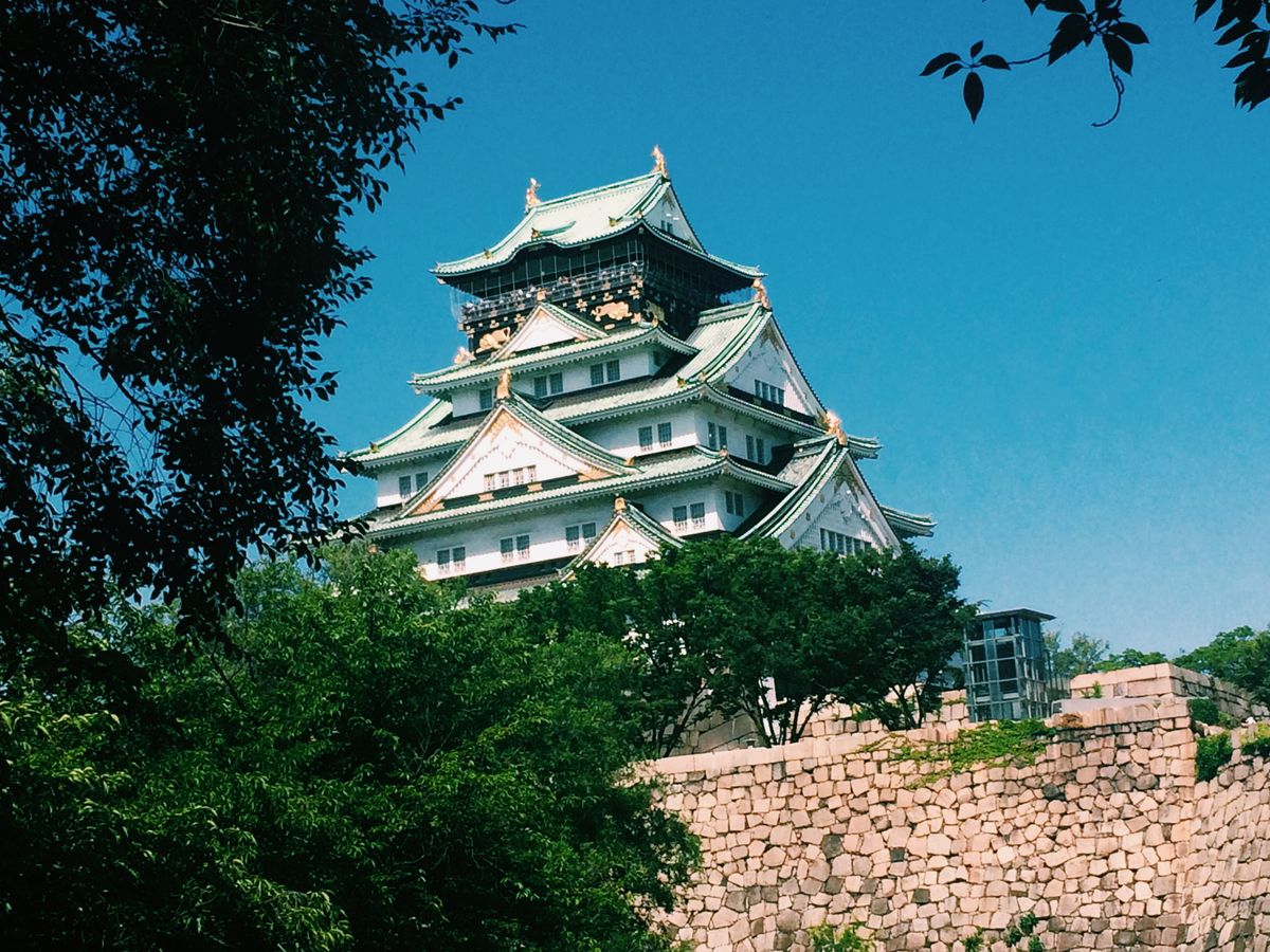 Osaka Castle tower surrounded by lush green trees on a sunny day