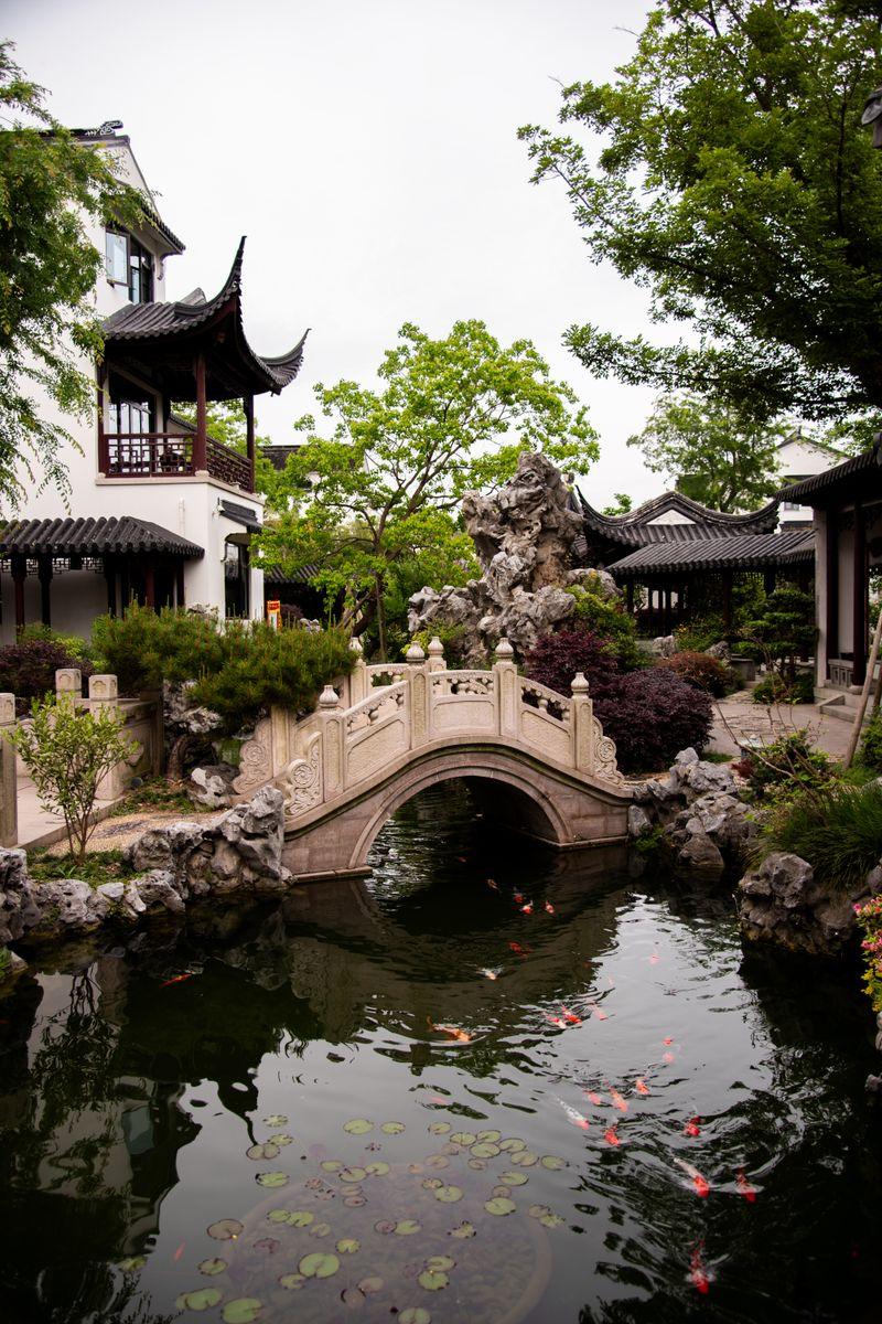 Classical Chinese garden zigzag stone bridge over a koi pond, in the style of Yu Garden's Sansui Hall area